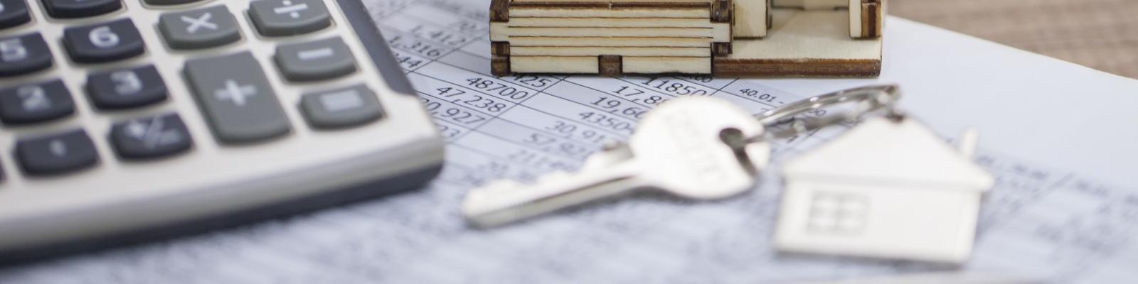 There is a small model home on a desk next to a calculator and new home key.