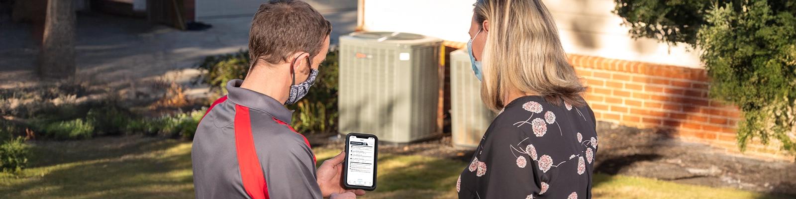Homeowner Talking to an HVAC Technician, Technician Is Holding a Smartphone with the Technician App Displayed